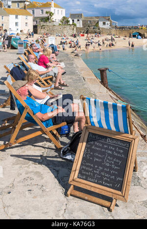 St Ives - Urlauber entspannen in Liegestühlen auf dem Kai am Hafen Strand St Ives Cornwall. Stockfoto