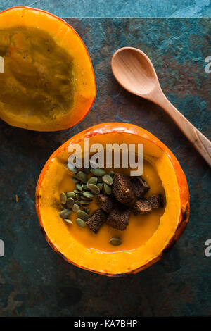 Kürbissuppe mit Samen und Croutons in einen Kürbis und ein Löffel vertikal Stockfoto