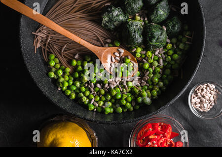 Buchweizen Nudeln in einer Pfanne, gefrorene Erbsen und Spinat, Chili und Samen in eine Schüssel horizontal Stockfoto