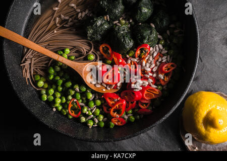 Buchweizen Nudeln, Erbsen und Spinat, Chili und Samen in einer Pfanne und auf grauem Stein horizontale Zitrone Stockfoto