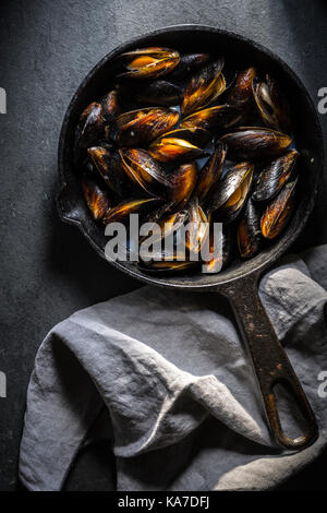 Muscheln auf einer gusseisernen Pfanne und Serviette auf einem grauen Hintergrund vertikal Stockfoto