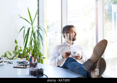 Geschäftsmann, der in seinem Büro, mit einer Unterbrechung, trinken Kaffee. Stockfoto