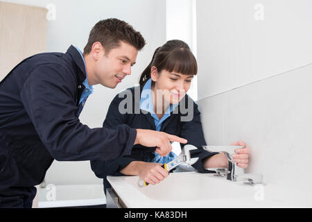 Weiblichen Auszubildenden Klempner Arbeiten am Wasserhahn im Badezimmer Stockfoto