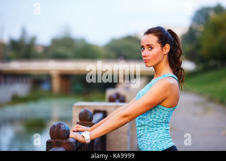 Portrait von jungen sportlichen Frau vor dem Joggen am Abend Stadt. Portrait von athletischen Mädchen in Blau top Entspannung nach Laufen bei Sonnenuntergang Stockfoto