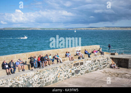 St Ives - Urlauber entspannen in der Sonne auf einem Kai in St. Ives in Cornwall. Stockfoto