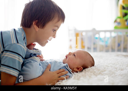 Schöne junge, umarmen mit Zärtlichkeit und sein neugeborenes Baby Bruder Pflege zu Hause. Familie Liebe Glück Konzept Stockfoto