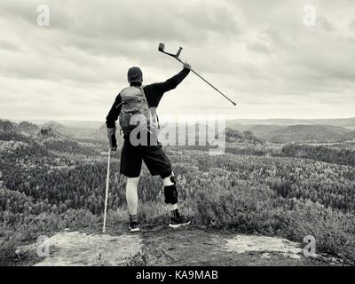 Behinderte Touristen auf Krücken auf Fels. Verletzte Knie in Neopren Metall knie Klammern und Mann halten die Unterarme stützen. Stockfoto