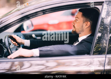 Portrait der junge Geschäftsmann, der ein Auto fährt, während die Kamera auf die Autobahn lächelnde Stockfoto