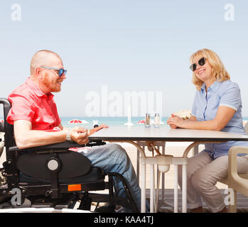 Junge behinderte Mensch sitzt eine Frau an einem Tisch am Strand Stockfoto