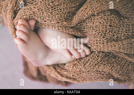 Schöne kleine Fersen eines neugeborenen Babys in einem braunen gestrickte Stück Stoff gewickelt Stockfoto