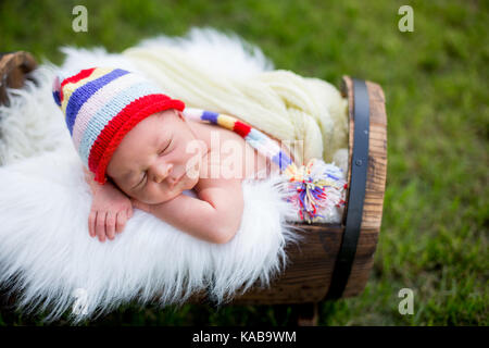 Wenig süßes neugeborenes Baby Boy, in der Kiste mit gestrickten bunten Hut im Garten schlafen, draußen im Park Stockfoto