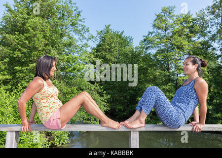Zwei Freunde gegenüber sitzt auf der Brücke Geländer Stockfoto
