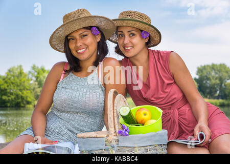 Zwei Freunde mit Hüten und Picknickkorb an Wasser in der Natur Stockfoto