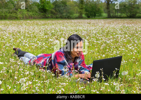 Kolumbianische Frau in der blühenden Wiese Arbeiten am Laptop liegen Stockfoto