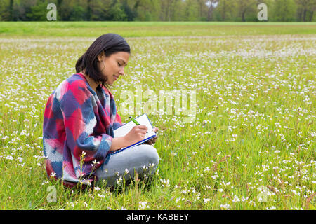 Kolumbianische Frau sitzt im niederländischen Wiese mit Blumen Stockfoto