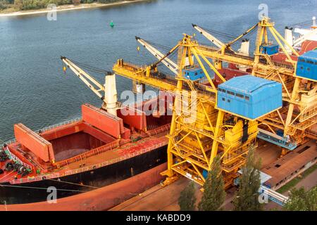 Kran entlädt Eisenerz in den Hafen. Der Handel mit Rohstoffen. Arbeiten an einem Port in der Ostsee Stockfoto