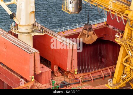 Kran entlädt Eisenerz in den Hafen. Der Handel mit Rohstoffen. Arbeiten an einem Port in der Ostsee Stockfoto