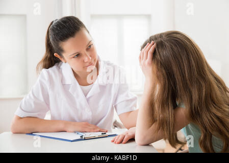 Ärztin tröstend Gedrückt am Tisch sitzenden Patienten Stockfoto