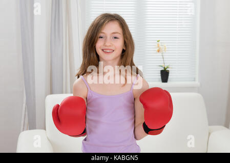 Happy girl das Tragen der roten Boxhandschuhe im Wohnzimmer Stockfoto
