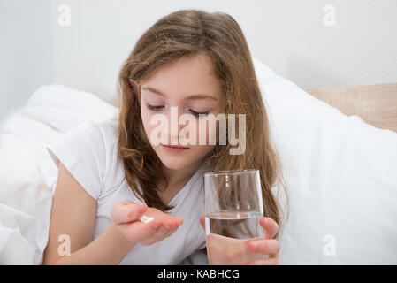 Mädchen auf dem Bett, die Tablette mit einem Glas Wasser im Schlafzimmer Stockfoto