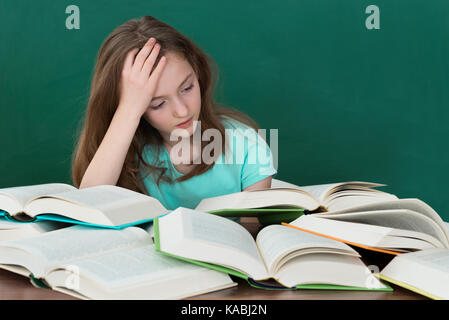 Mädchen mit vielen offenen Bücher am Schreibtisch im Klassenzimmer umgekippt Stockfoto