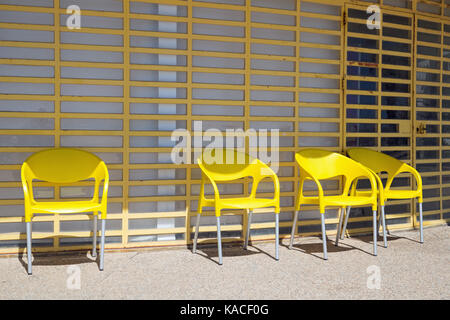 Vier gelbe Plastikstühle Schuß gegen eine gelbe vergitterten Fenster Stockfoto