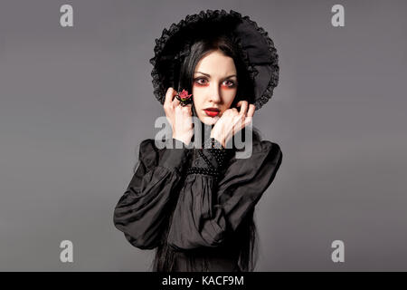 Portrait von brünette Frau im schwarzen Kleid und klassische gotische Stil mit roten Augen auf grauem Hintergrund. halloween Konzept. Stockfoto