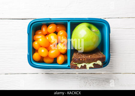 Bild von Cherry Tomate, Apfel, Sandwich in der Brotdose auf weissem Holztisch, Stockfoto