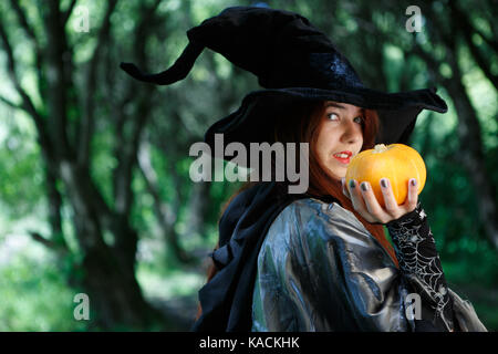 Portrait von Hexe in schwarzen Hut mit Kürbis von Angesicht zu mystischen Wald Stockfoto