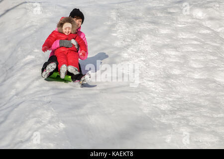 Glückliche Mutter und ihrer Tochter mit einer Schlittenfahrt hinunter den Hügel, winter Spiele und Spaß. Urlaub mit der Familie und Zweisamkeit. Stockfoto