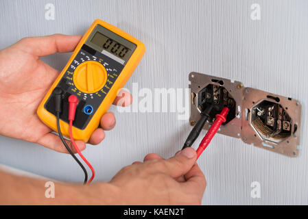 Nahaufnahme der Person Hand Sockel Spannung mit Multimeter prüfen. Stockfoto