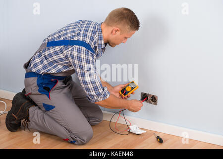 Männliche Elektriker Prüfung der Spannung der Steckdose mit Multimeter im Haus Stockfoto