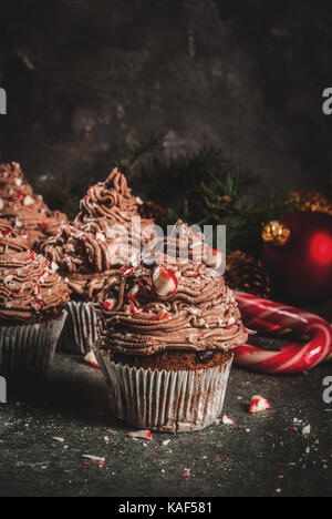 Weihnachten Süßigkeiten und Desserts, Schokolade Pfefferminz Cupcakes mit Zuckerstange Krümel, auf schwarzen Hintergrund mit Weihnachtsbaum und Kugeln, Kopie Raum Stockfoto