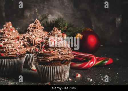 Weihnachten Süßigkeiten und Desserts, Schokolade Pfefferminz Cupcakes mit Zuckerstange Krümel, auf schwarzen Hintergrund mit Weihnachtsbaum und Kugeln, Kopie Raum Stockfoto