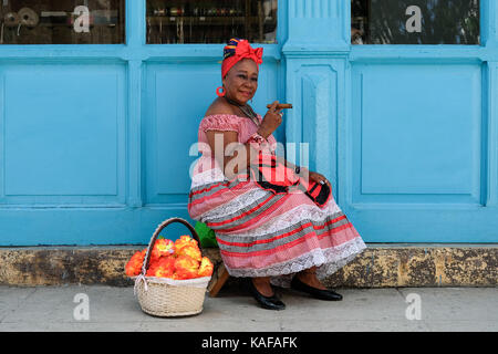 Ein farbenfroh gekleideten kubanische Frau in traditioneller Kleidung sitzt auf den Straßen von Habana Vieja in Havanna, Kuba. Stockfoto