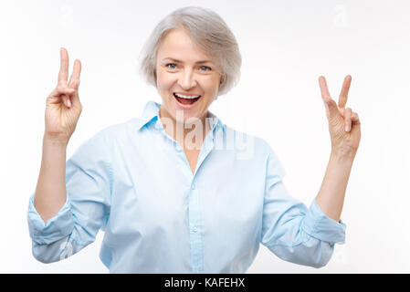 Fröhliche grauhaarige Frau, v-Zeichen mit beiden Händen Stockfoto