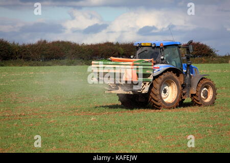 Ein Bauer Verbreitung Dünger über eine vor kurzem gepflügten Feldes mit einem Traktor angehängten Maschine mit drehenden Scheiben die Chemikalien zu verteilen. Stockfoto