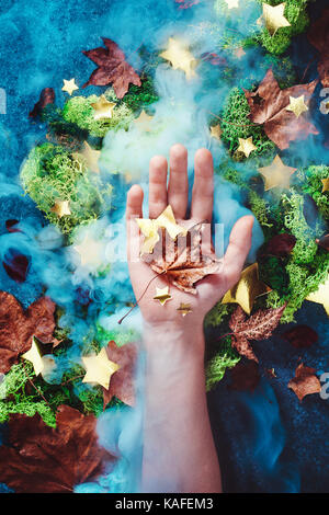 Hand mit einem maple leaf auf einem Herbst Hintergrund mit Moos, Laub, goldene Sterne und Rauch. Konzeptionelle Herbst noch leben. Stockfoto