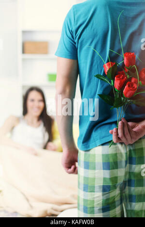 Mann gibt einer Frau eine Rose im Bett, als Zeichen der Liebe und Aufmerksamkeit Stockfoto