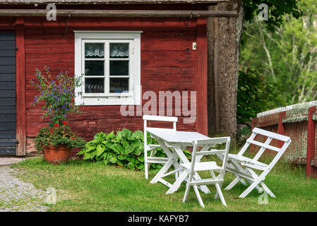 Weiß Holz Gartenmöbel außerhalb eines roten traditionelle Scheune Fenster. Blumentopf und Blumenbeet Außerhalb der Scheune. Stockfoto