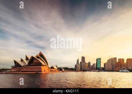 Sydney, Australien - 10. November 2015: Opernhaus mit Sydney Skyline der Stadt bei Sonnenuntergang. Blick von der Fähre nähert sich Circular Quay. Stockfoto