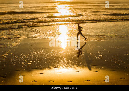 Mann laufen am Strand bei Sonnenaufgang. Großbritannien Stockfoto