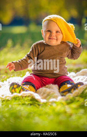 Nettes glückliches Kind Baby spielt mit gelber Mütze Hut im Herbst Sonne Stockfoto