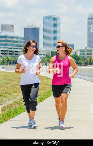 Zwei Frauen Joggen entlang der Bayshore Boulevard mit der Innenstadt von Tampa, Florida, USA Skyline im Hintergrund. Stockfoto