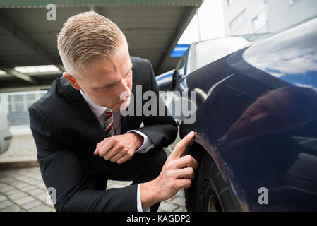 Portrait des jungen Mannes auf der Suche nach Kratzer auf seinem Auto Stockfoto