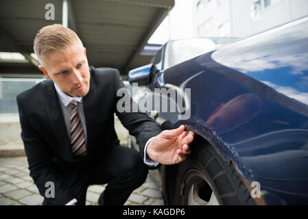 Portrait des jungen Mannes auf der Suche nach Kratzer auf seinem Auto Stockfoto