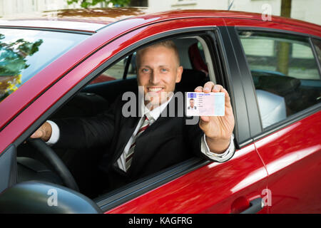 Portrait einer jungen Geschäftsmann, der seine Führerschein aus dem offenen Autofenster Stockfoto