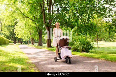 Glückliche Mutter mit Kind im Kinderwagen im Summer Park Stockfoto