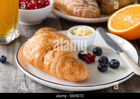 Kontinentales Frühstück mit frischen Croissants, Butter, ein Glas Orangensaft, Marmelade und Obst auf Holztisch. Detailansicht, horizontal Stockfoto