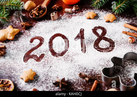 Frohes neues Jahr 2018 Geschrieben von Mehl und Weihnachtsschmuck Lebkuchen cookies, Cinnamin, Orangen, Gewürzen, Nüssen und Ausstechformen auf hölzernen Hinterg Stockfoto